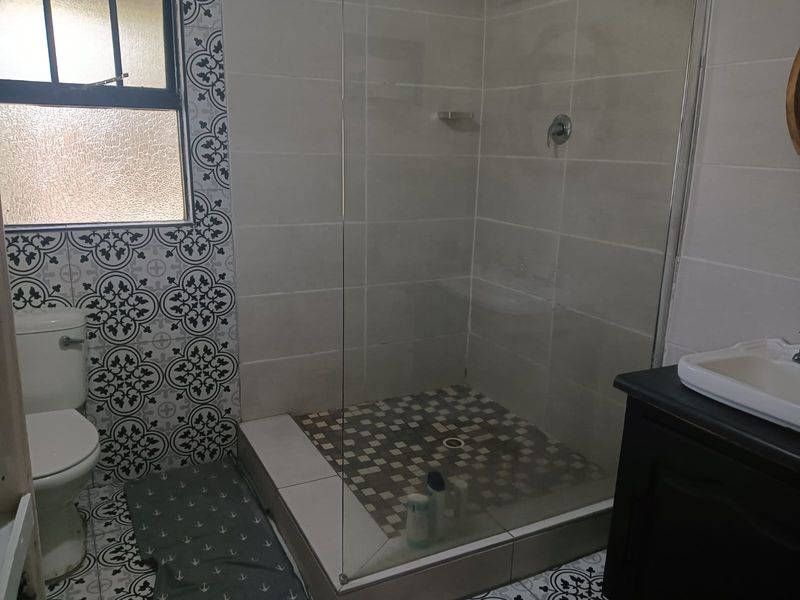 A modern bathroom featuring a walk-in shower with a glass screen, patterned floor tiles, a toilet, and a vanity basin.
