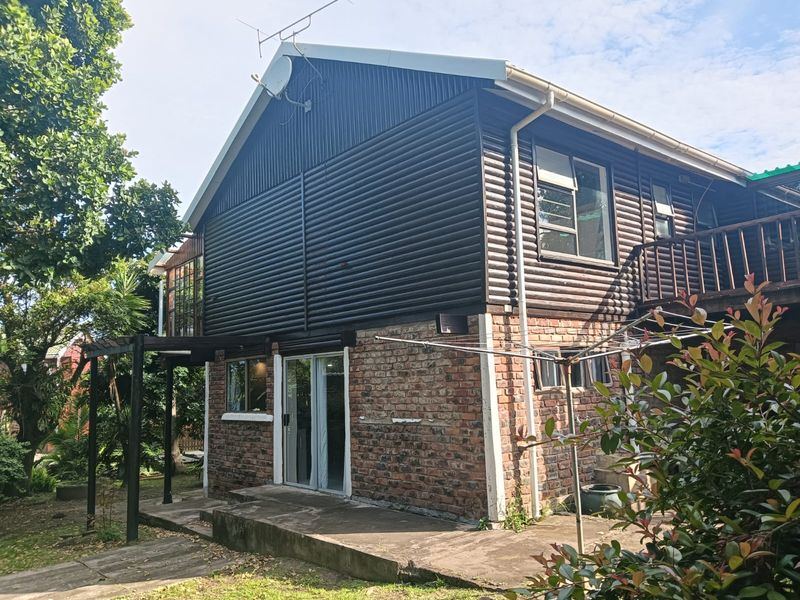 Rear view of a two-story house featuring a combination of brick and timber cladding, a concrete patio, and an upper-level wooden balcony.