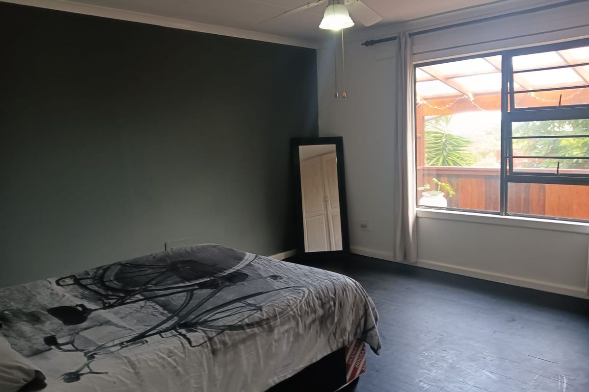 A bedroom featuring a dark accent wall, dark timber flooring, and a ceiling fan, with natural light provided by a large window.