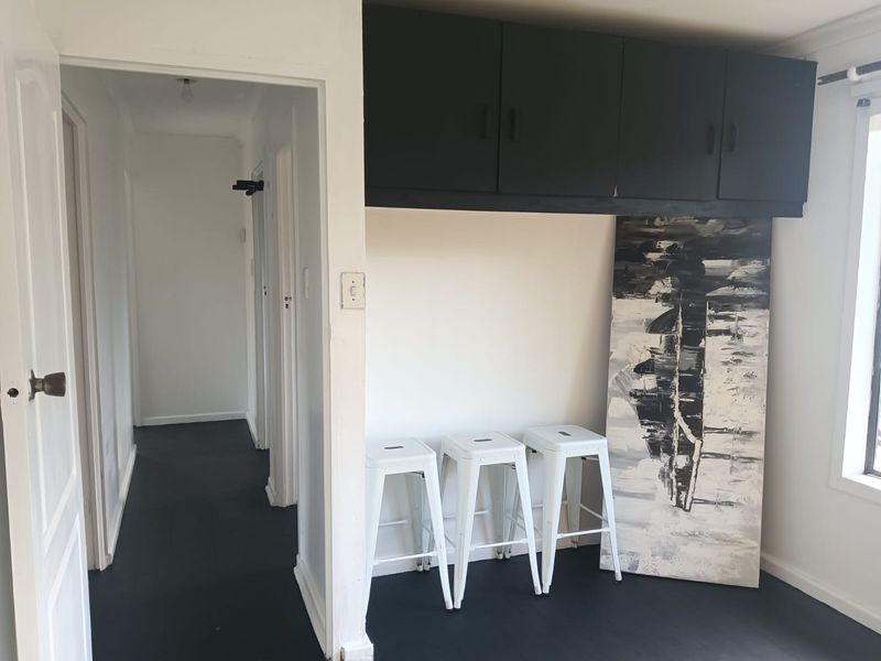 A living area featuring built-in overhead storage cabinetry and dark painted flooring, leading into a hallway.