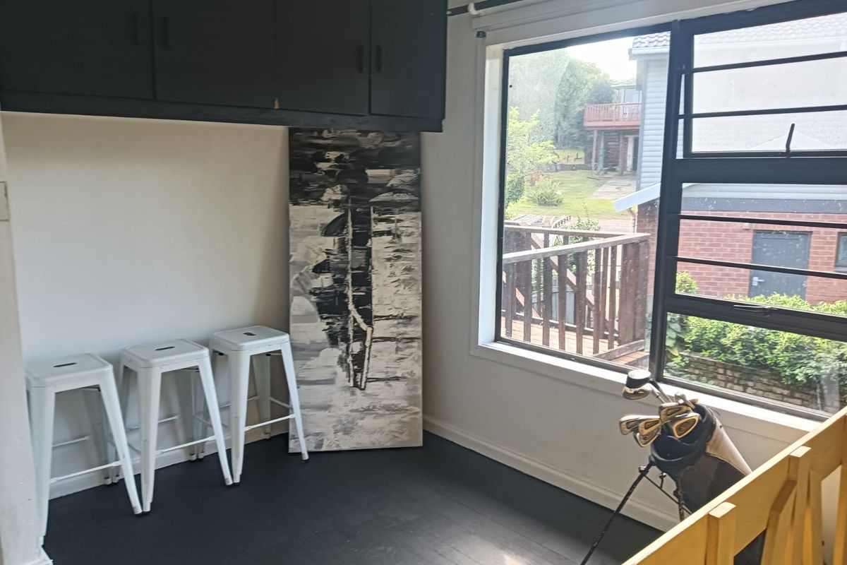 A living area featuring built-in overhead cabinetry, dark timber flooring, and a large window overlooking the exterior.