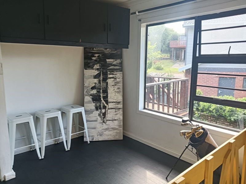 A living area featuring built-in overhead cabinetry, dark timber flooring, and a large window overlooking the exterior.