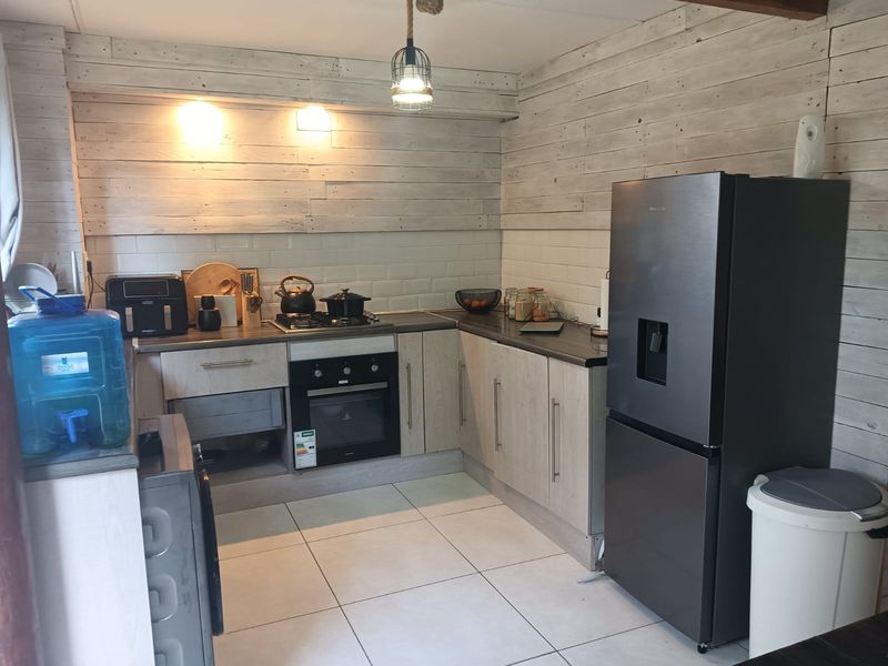 A functional kitchen featuring light-toned laminate cabinetry, subway tile backsplash, timber wall cladding, and built-in oven with gas hob.
