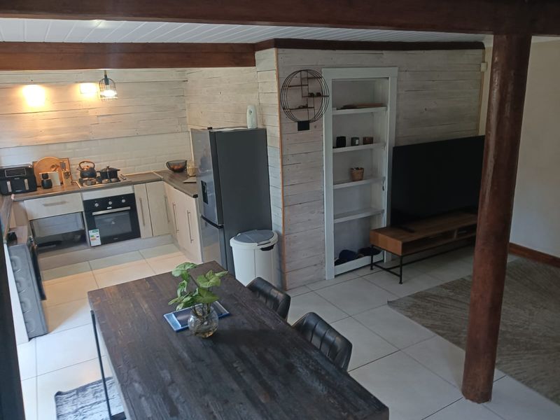 Open-plan living and kitchen area featuring tiled floors, timber ceiling beams, rustic wall cladding, and a functional kitchen with built-in appliances.