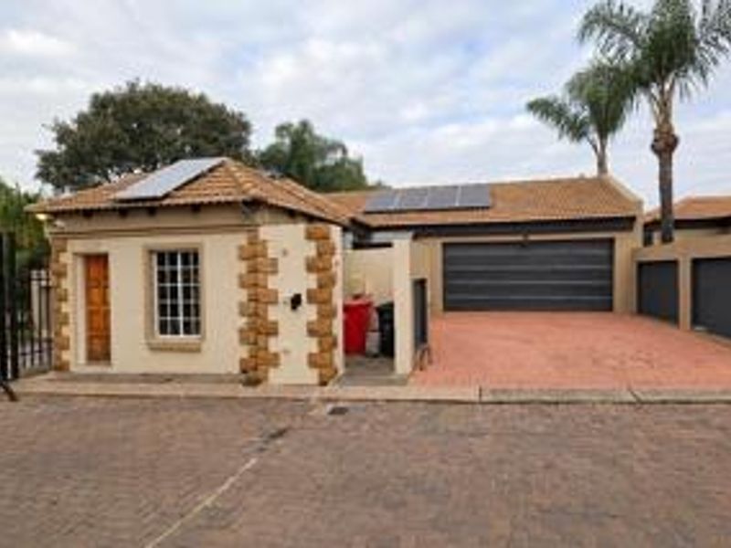 Front elevation of a residential property featuring a tiled roof with solar panels, stone-clad accents, and a paved driveway leading to a double garage.