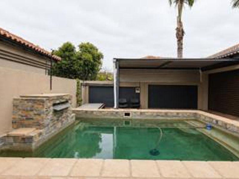 Outdoor pool area featuring a stone-clad water feature, a covered patio space with roller shutters, and tiled pool coping.