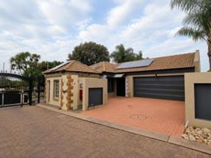 Front exterior view of the property featuring a paved driveway, double garage, solar panels, and secure gated entrance.