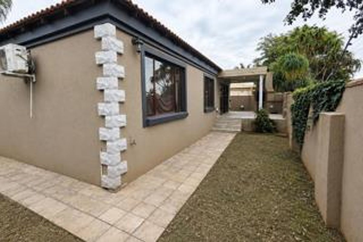 Rear exterior view of the house featuring a paved patio area, stone corner detailing, and a well-maintained boundary wall.