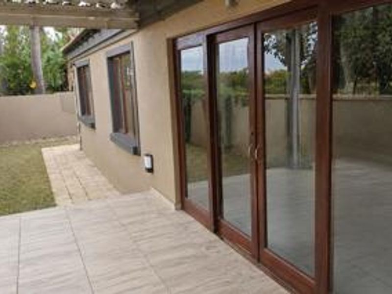 A covered patio area featuring tiled flooring and large sliding glass doors, providing seamless access to the outdoor garden space.