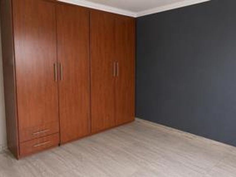 A clean, empty bedroom featuring modern laminate flooring, a dark accent wall, and extensive built-in wooden cupboards.