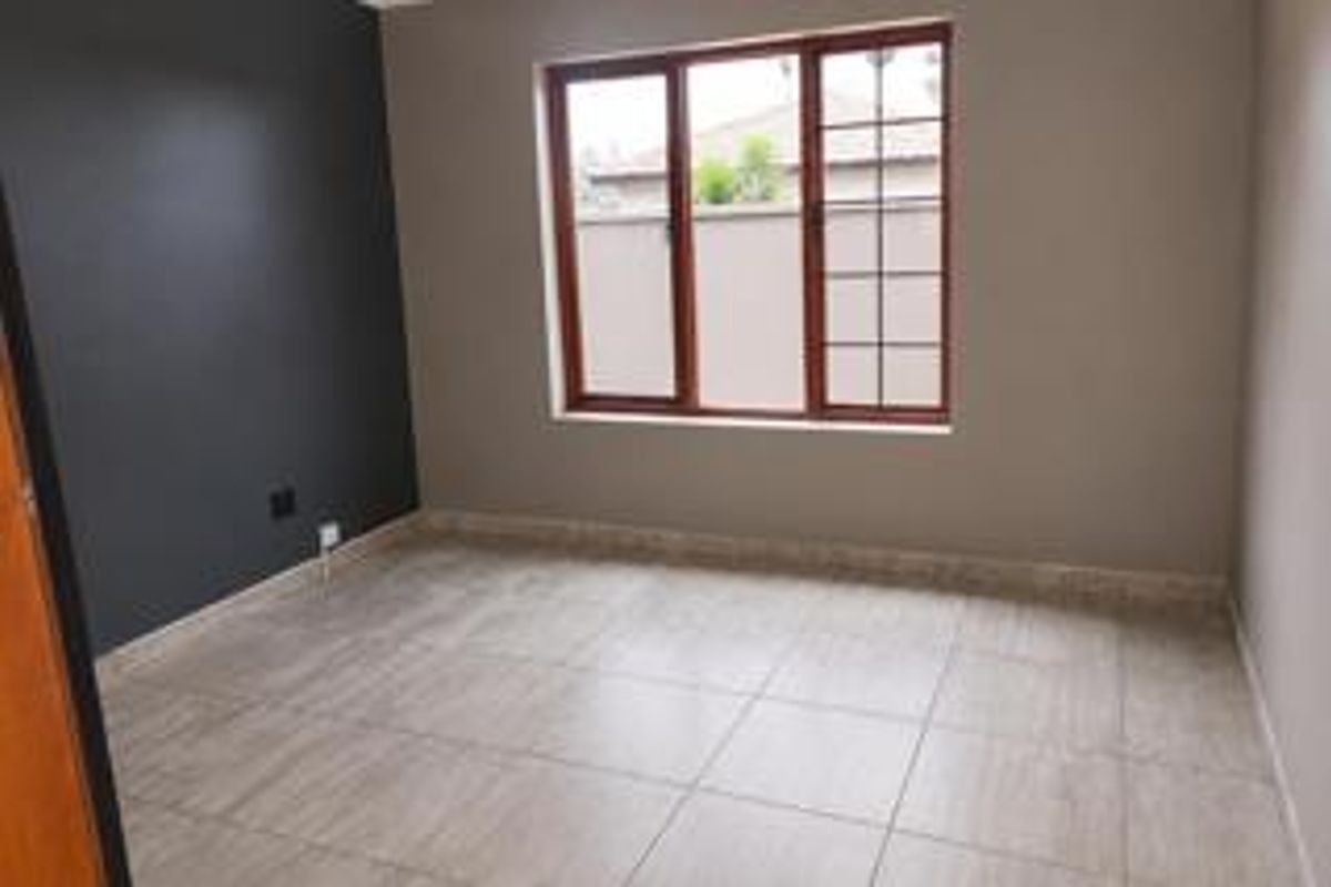 A clean, empty bedroom featuring neutral tiled flooring, a dark accent wall, and wooden window frames providing natural light.
