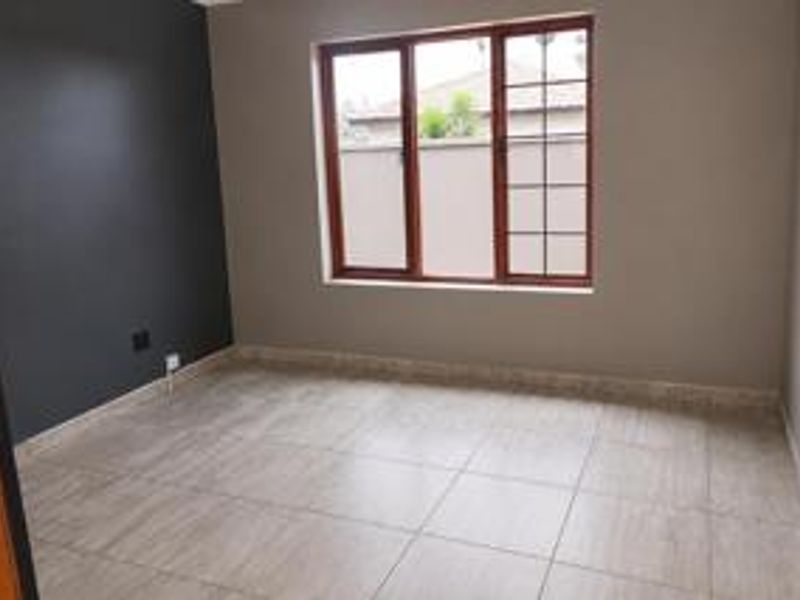 A clean, empty bedroom featuring neutral tiled flooring, a dark accent wall, and wooden window frames providing natural light.