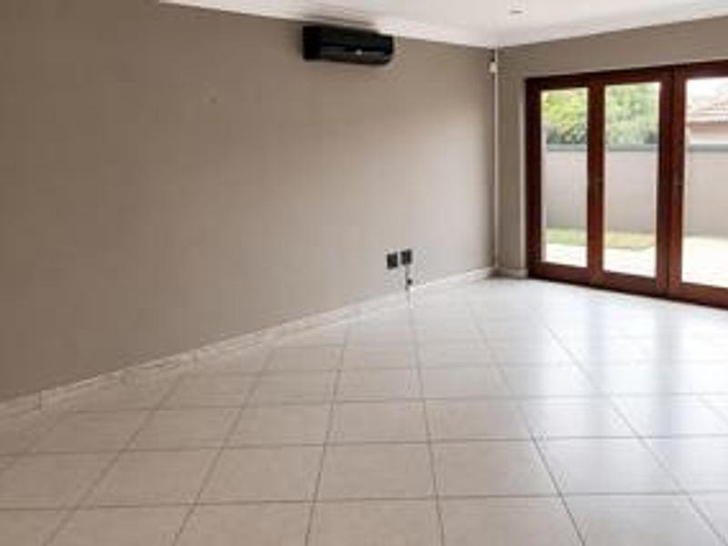 A spacious, empty living area featuring neutral tiled flooring, an installed air conditioning unit, and large wooden folding doors leading to the exterior.