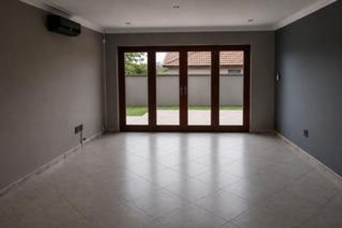 A spacious, empty living room featuring tiled flooring, recessed lighting, and large bi-fold doors providing direct access to the rear patio and garden.
