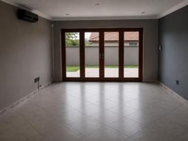 A spacious, empty living room featuring tiled flooring, recessed lighting, and large bi-fold doors providing direct access to the rear patio and garden.
