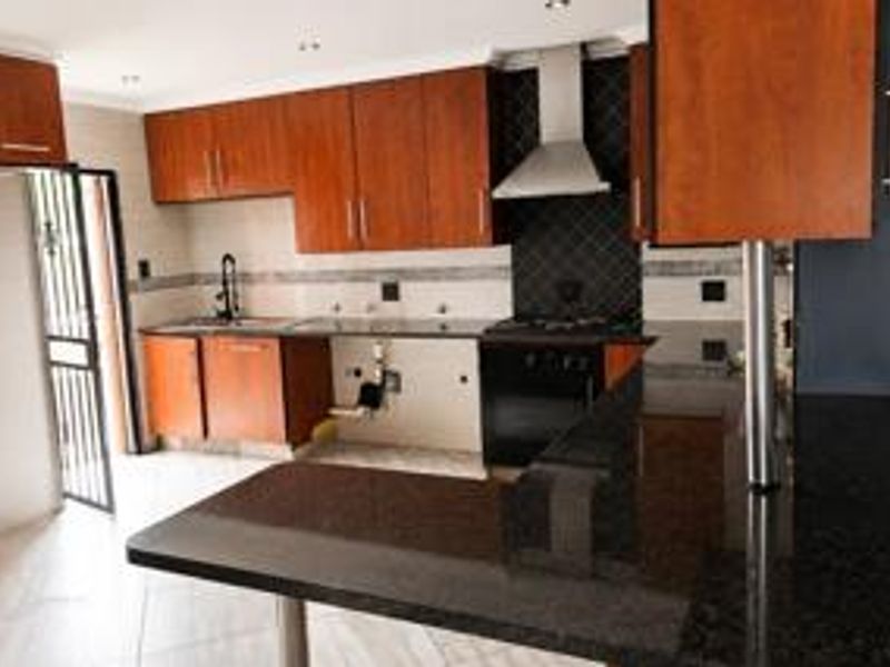 A functional kitchen featuring wooden cabinetry, granite countertops, a breakfast bar, and built-in cooking appliances, with an adjacent security door leading outside.