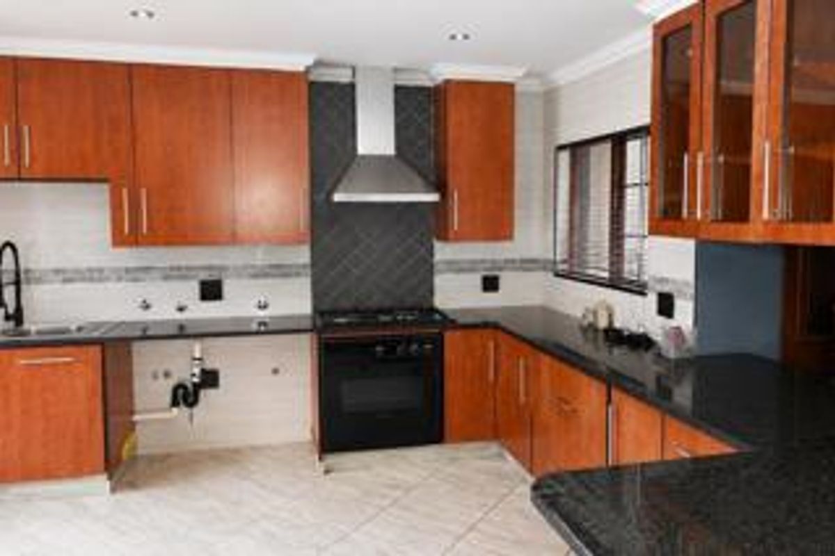A functional kitchen featuring wooden cabinetry, granite countertops, a gas hob, and a stainless steel extractor fan, with tiled flooring throughout.