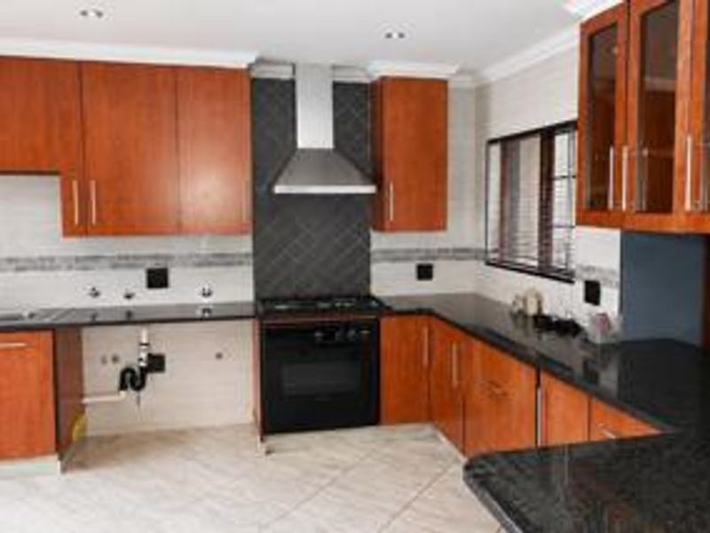 A functional kitchen featuring wooden cabinetry, granite countertops, a gas hob, and a stainless steel extractor fan, with tiled flooring throughout.