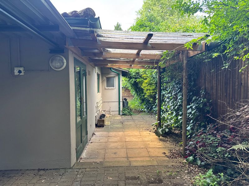A covered outdoor patio area featuring a timber pergola structure, paved flooring, and direct access to the cottage exterior.