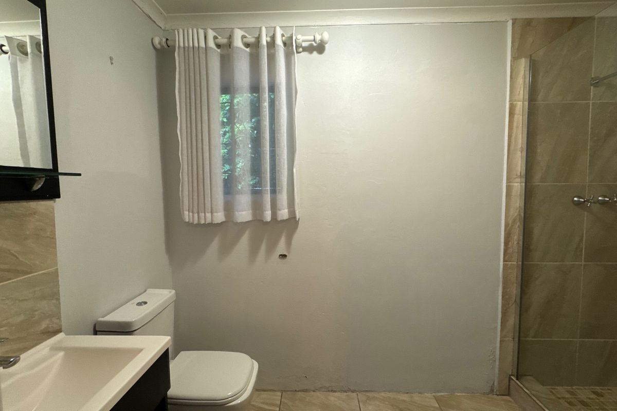 A functional bathroom featuring a tiled shower enclosure, modern vanity, and toilet, with some minor wall finishing required.