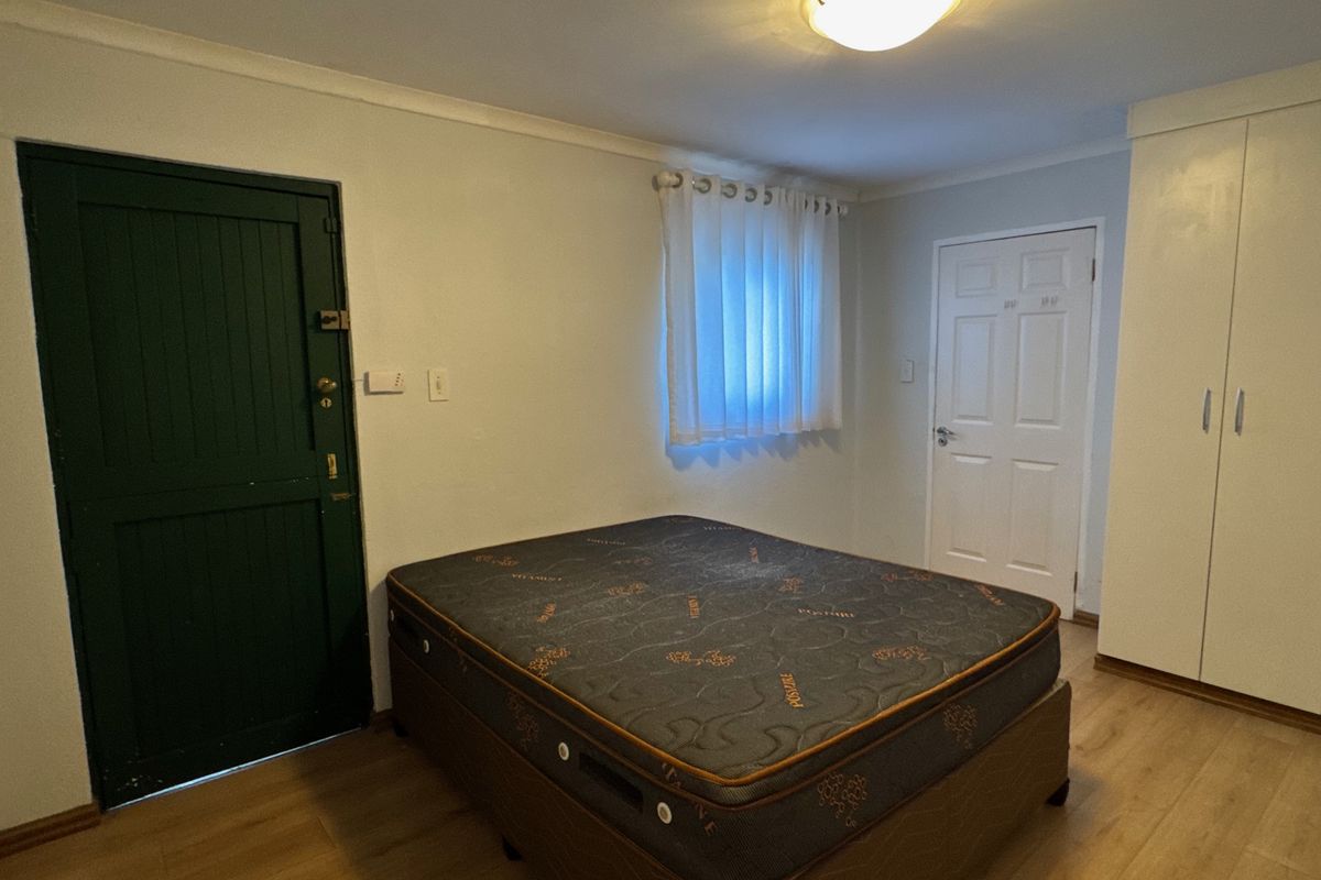 A functional bedroom featuring laminate flooring, a built-in wardrobe, and a ceiling light fixture, offering a clean and neutral space.