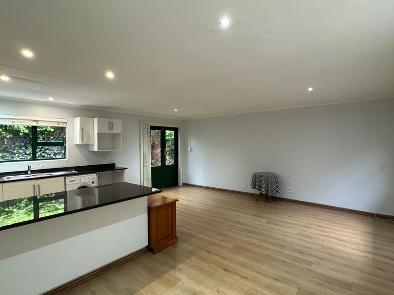 Spacious open-plan living area featuring modern laminate flooring, recessed lighting, and a functional kitchen with sleek black granite countertops and direct garden access.