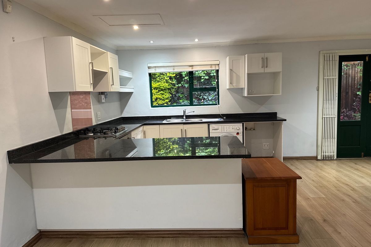 A functional kitchen featuring white cabinetry, dark granite countertops, a gas hob, and laminate flooring, with direct access to the rear garden.