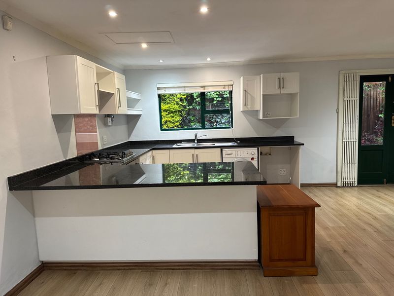 A functional kitchen featuring white cabinetry, dark granite countertops, a gas hob, and laminate flooring, with direct access to the rear garden.