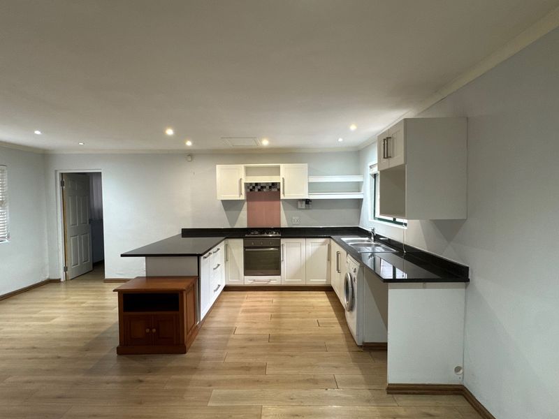 Spacious open-plan kitchen featuring white cabinetry, black granite countertops, built-in oven, gas hob, and integrated laundry plumbing, finished with modern laminate flooring.