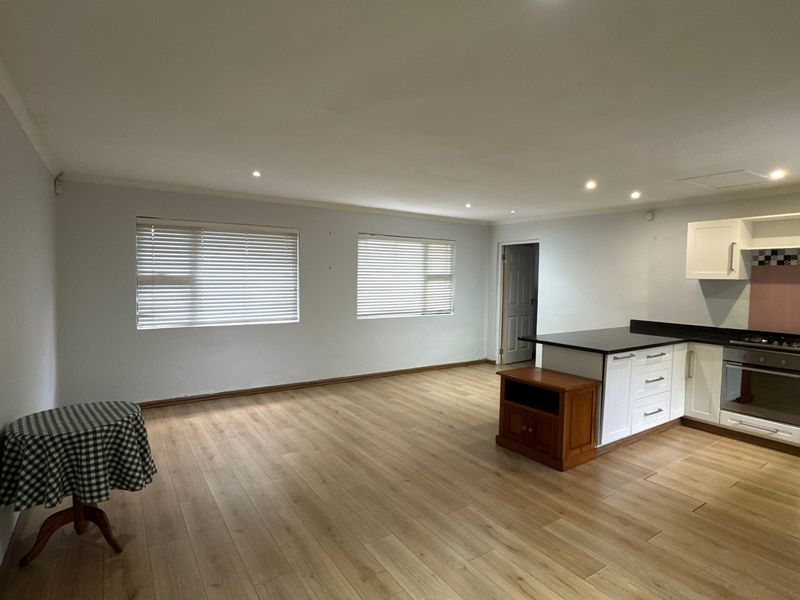 Spacious open-plan living area featuring laminate flooring, recessed lighting, and a modern kitchen with built-in appliances and ample cabinetry.