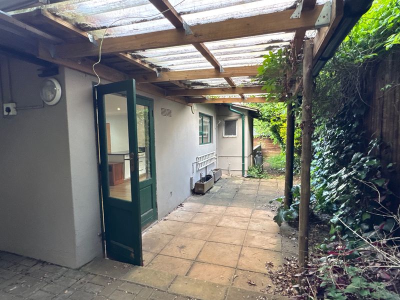 A covered outdoor patio area featuring a timber pergola with corrugated roofing, providing a sheltered transition space between the garden and the interior.