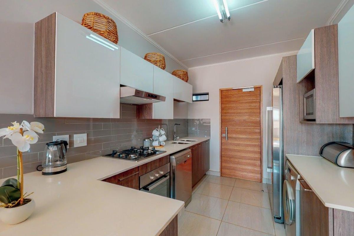 Modern kitchen featuring sleek white and wood-tone cabinetry, stone countertops, gas hob, integrated oven, and tiled backsplash with neutral floor tiles.
