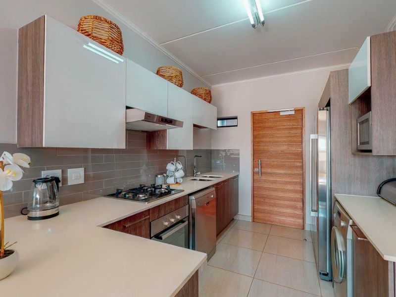 Modern kitchen featuring sleek white and wood-tone cabinetry, stone countertops, gas hob, integrated oven, and tiled backsplash with neutral floor tiles.