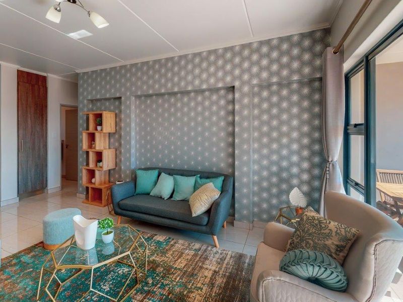 An open-plan living area featuring tiled floors, a decorative wallpapered feature wall, and seamless access to an adjoining balcony through large sliding glass doors.