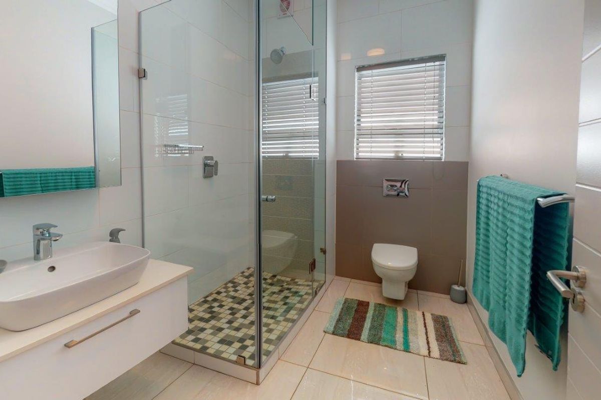 Modern bathroom featuring a wall-mounted vanity with vessel sink, glass-enclosed shower, and wall-hung toilet with neutral tile finishes.