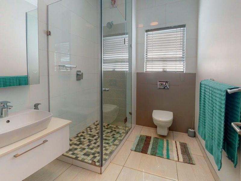 Modern bathroom featuring a wall-mounted vanity with vessel sink, glass-enclosed shower, and wall-hung toilet with neutral tile finishes.