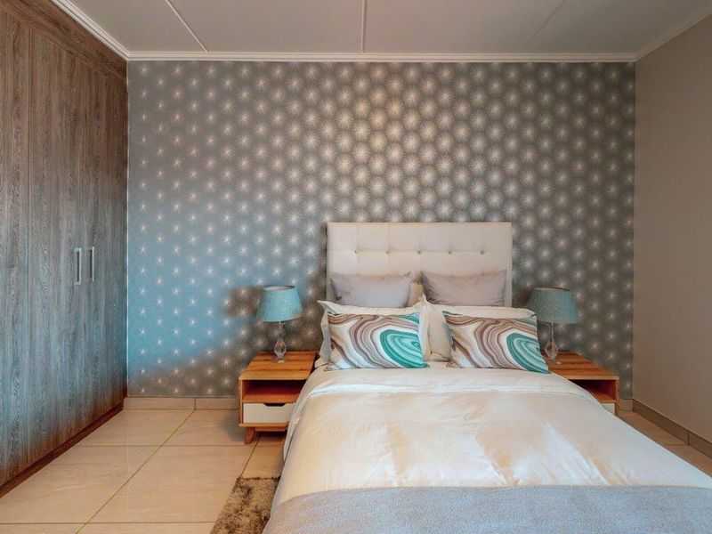 A well-maintained bedroom featuring built-in cupboards, tiled flooring, and a decorative feature wall.