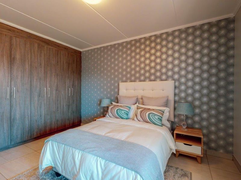 A well-maintained bedroom featuring extensive built-in wooden cupboards, neutral tiled flooring, and a decorative feature wall.