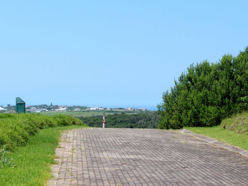 A view of a paved residential driveway leading towards a scenic landscape with distant coastal views.