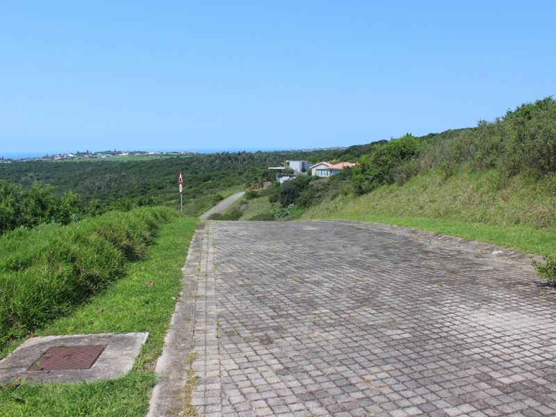 A view looking down a paved residential driveway towards the surrounding landscape and distant coastal area.