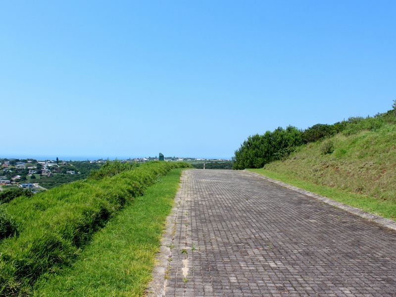 A view of a paved driveway leading towards a coastal landscape with residential properties in the distance.