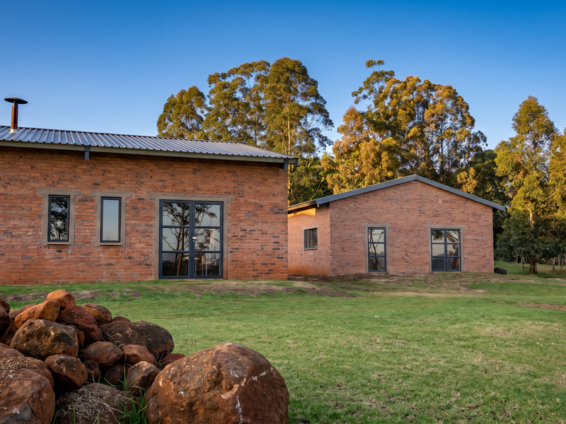 Rear view of a modern industrial-style brick dwelling featuring large glass doors, aluminium windows, and a corrugated metal roof set in a landscaped garden.