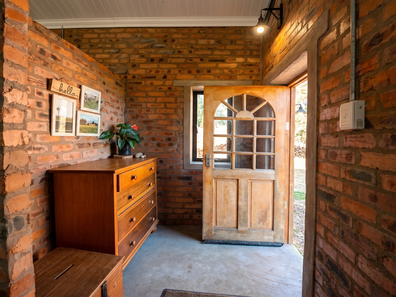 Rustic entryway featuring exposed brick walls, concrete flooring, and a classic timber panelled door with exposed electrical conduit detailing.