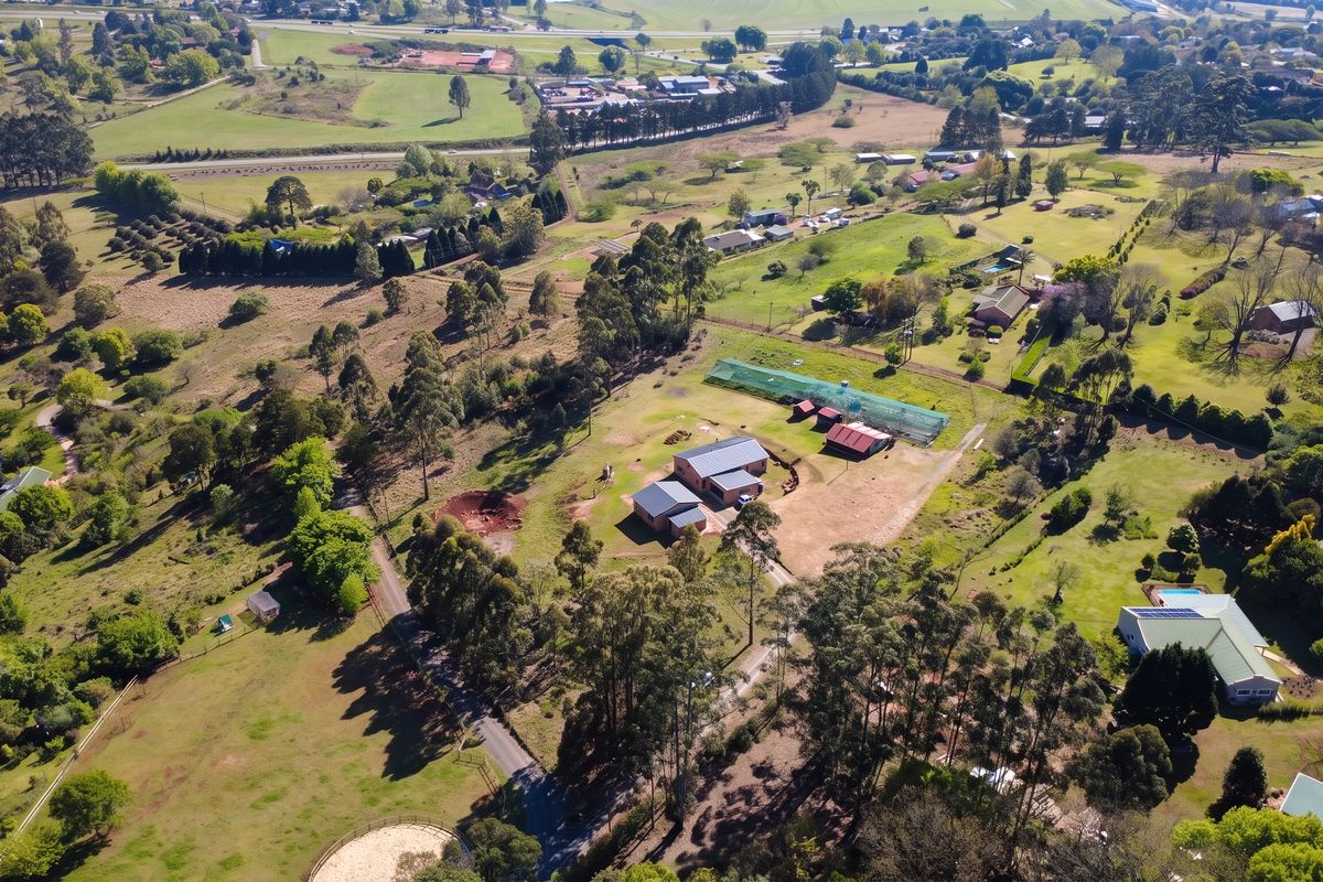Aerial view of a small holding property featuring multiple outbuildings, a greenhouse, and extensive landscaped grounds with mature trees and established fencing.
