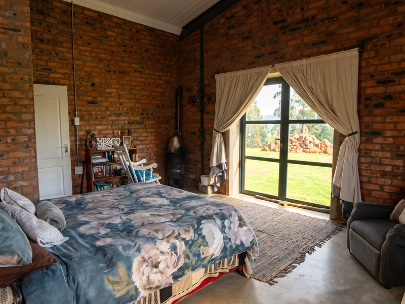 Spacious bedroom featuring rustic exposed brick walls, concrete flooring, a wood-burning stove, and large glass doors providing direct access to the garden.
