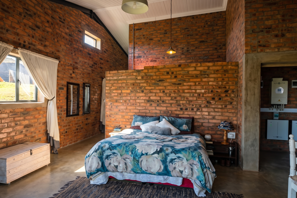 Spacious bedroom featuring rustic exposed brick walls, vaulted ceilings, polished concrete floors, and an integrated solar power system in the adjacent utility area.