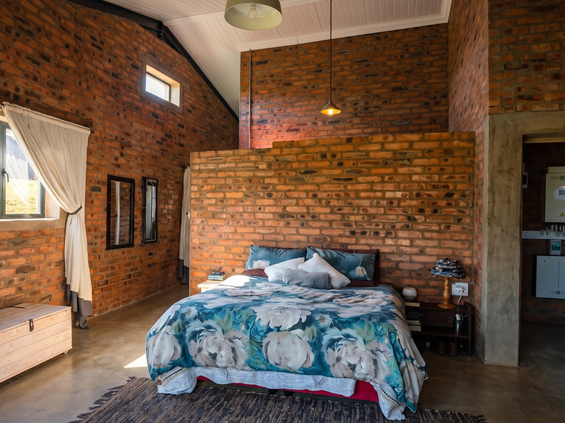 Spacious bedroom featuring rustic exposed brick walls, vaulted ceilings, polished concrete floors, and an integrated solar power system in the adjacent utility area.