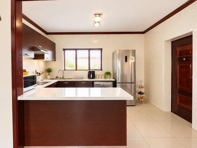 A well-maintained kitchen featuring dark wood cabinetry, white stone countertops, tiled backsplash, and modern stainless steel fixtures in a clean, functional layout.