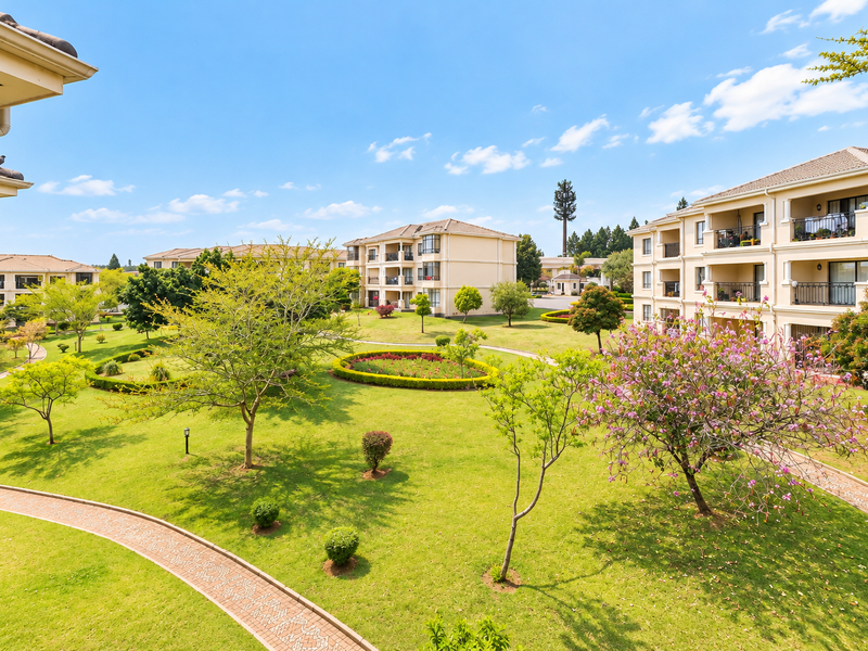A view of the well-maintained communal gardens and landscaped grounds between the apartment buildings, featuring paved walkways and mature trees.