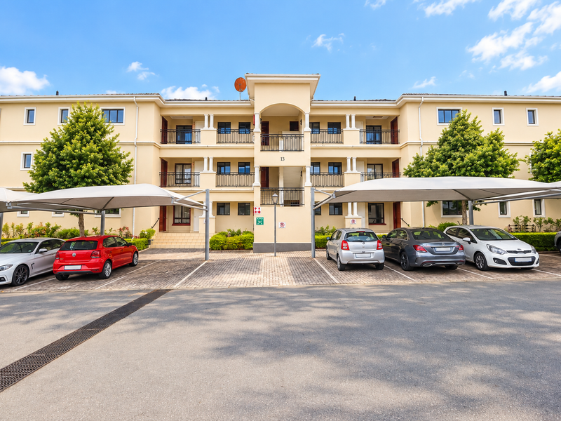 Front elevation of a multi-story apartment complex featuring covered parking bays, paved driveway, and private balconies for each unit.
